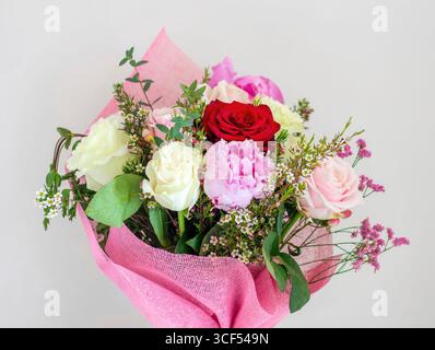 Beau bouquet de roses roses, blanches et rouges et de pivoines enveloppé dans un papier rose, parfait pour une célébration ou un cadeau, créant une atmosphère romantique et festive Banque D'Images