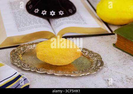 1er août 2025 Jérusalem Israël fête juive traditionnelle etrog agrumes sur livre de prière ouvert avec texte hébreu, kippa avec étoile de David pour la célébration de Sukkot etrog, livre de prière châle de prière traditionnel Tanakh livre sacré de prière Banque D'Images