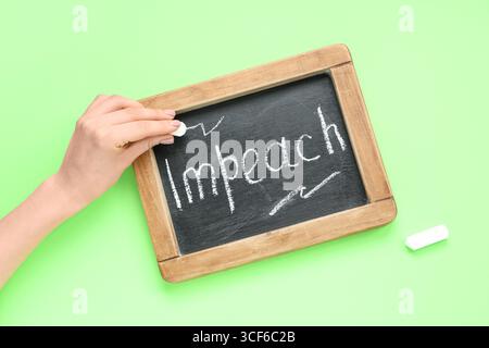 Femme écrivant le mot IMPEACH sur le tableau noir sur fond vert Banque D'Images