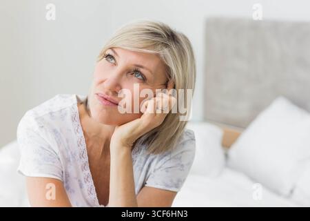 Femme senior reposant la tête sur la main et regardant vers le haut dans la chambre avec la literie blanche montrant anneau Banque D'Images