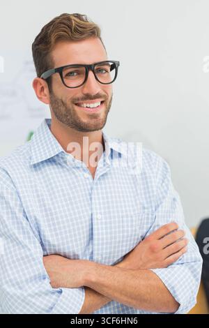 Homme debout avec les bras croisés dans la salle de conférence portant des lunettes à côté des griffonnages du tableau blanc Banque D'Images