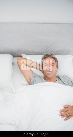 Homme allongé sur le lit dans la chambre, reposant sous couette blanche avec oreiller et tête de lit matelassée Banque D'Images