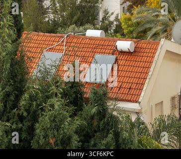 Gros plan sur le toit de la maison avec des panneaux solaires et des chauffe-eau entourés d'arbres verts. Concept d'écologie, de durabilité et d'énergie alternative Banque D'Images