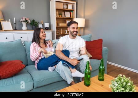 Jeune homme de couple et femme assis à la maison sur le canapé prenant une pause après une journée de travail stressante regarder un jeu de sport ou un film à la télévision, manger du pop-corn et du drin Banque D'Images
