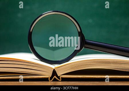 Un livre ouvert repose sur une surface en bois avec une loupe positionnée sur le texte, mettant l'accent sur la recherche en éducation et l'analyse de détails spécifiques. Banque D'Images