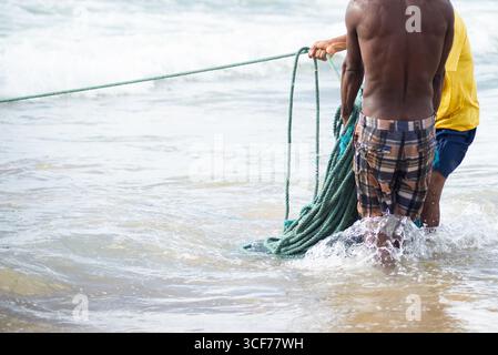 Un demi-corps de pêcheurs non identifiés ramassant le filet de pêche après avoir capturé du poisson. Fruits de mer, pêche comme passe-temps. Brésil Banque D'Images