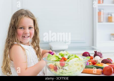 Enfant femelle tenant l'éplucheur et hachant la laitue dans un saladier sur le comptoir de la cuisine, copier l'espace Banque D'Images