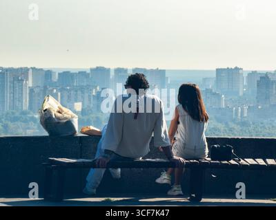 Kiev, Ukraine - 20 juillet 2025 : touristes assis sur un banc, profitant de l'horizon urbain depuis un point de vue élevé dans le Parc de la gloire éternelle, Kiev, par une journée ensoleillée Banque D'Images