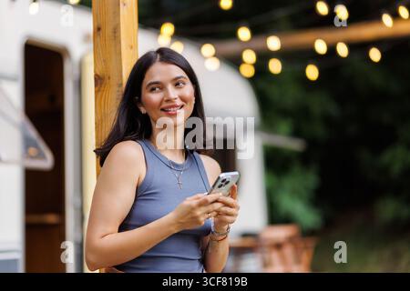 Jeune jolie femme utilise le téléphone devant le camping-car loué en vocation Banque D'Images