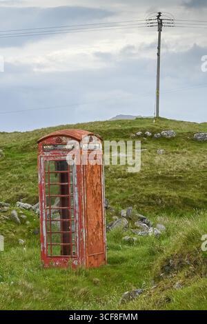 North Uist Scotland UK 06.18.2025 boîte téléphonique rouge emblématique pourriture abandonnée sur landes vertes par route de landes sur le bord du village avec des lignes électriques et des poteaux beh Banque D'Images