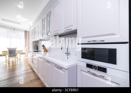 Une cuisine avec des armoires blanches et un évier blanc. L'évier est à côté d'un micro-ondes et d'un grille-pain Banque D'Images