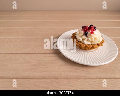 Une image en gros plan d'une délicieuse tarte aux baies avec une croûte brun doré, recouverte de crème blanche et d'un mélange de bleuets frais et de groseilles rouges, placée Banque D'Images