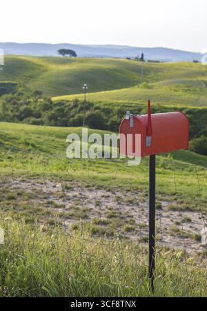Boîte aux lettres debout rouge dans un champ avec des collines verdoyantes en arrière-plan, Toscane, Italie Banque D'Images