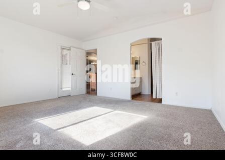 Cette chambre lumineuse et spacieuse dispose de moquette, d''un ventilateur de plafond et d''une salle de bains attenante. Idéal pour le home staging ou les annonces immobilières. Banque D'Images