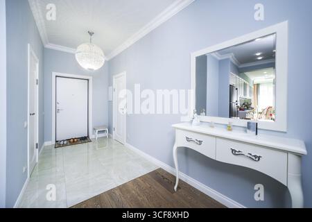 Un grand miroir blanc est sur une commode blanche dans un couloir. Le couloir est décoré avec un thème de couleur blanche et a une porte blanche Banque D'Images