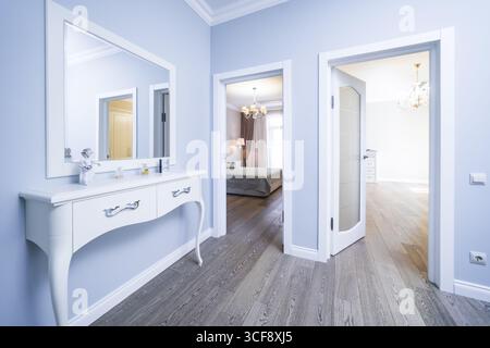 Un grand miroir blanc est sur une commode blanche dans un couloir. Le couloir est décoré avec un thème de couleur blanche et a une porte blanche Banque D'Images