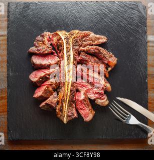 Steak grillé et tranché en T-bone avec assaisonnements sur une assiette de service en ardoise. Pose à plat. Banque D'Images