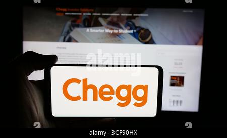 Stuttgart, Allemagne - 08-18-2025 : personne tenant un téléphone portable avec le logo de la société américaine de edtech Chegg Inc. sur l'écran en face de la page Web. Banque D'Images