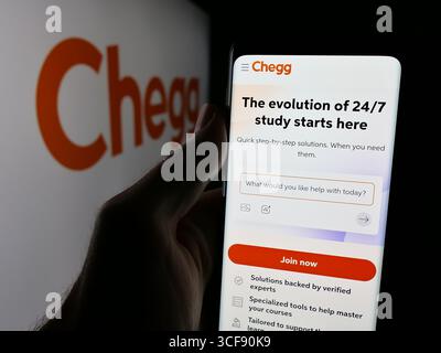 Stuttgart, Allemagne - 08-18-2025 : personne tenant le téléphone portable avec la page Web de la société américaine de edtech Chegg Inc. sur l'écran devant le logo. Banque D'Images