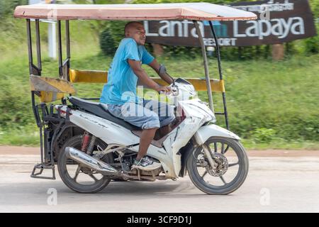KOH LANTA, THAÏLANDE, DEC 01 2024, Un homme monte un taxi moto vide à trois roues sur une route rurale Banque D'Images