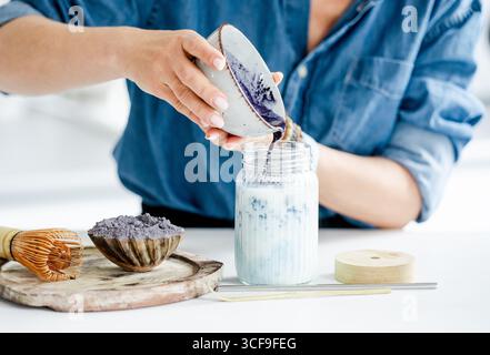 Femme verse Un latte Matcha glacé bleu dans Un pot avec de la glace et du lait Banque D'Images