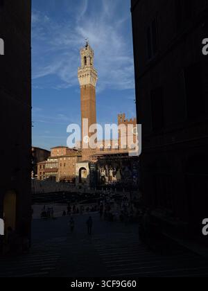 Touristes se relaxant pendant la soirée d'été dorée sur la Piazza del Campo, Sienne historique, Torre del Mangia silhouettée sur fond bleu Azur dynamique Banque D'Images