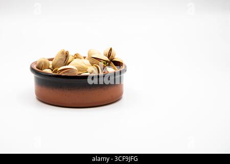 Petit plat en terre cuite rempli de pistaches sur un fond blanc propre, parfait pour illustrer des collations saines, la nutrition et la nourriture naturelle Banque D'Images