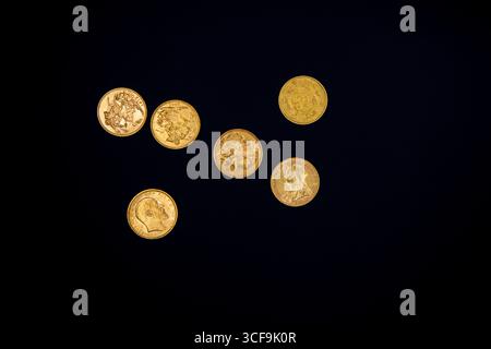 Six pièces souveraines en or disposées sur un fond noir, photographiées d'en haut, mettant en évidence leurs détails, leur brillance et leur design historique. Banque D'Images