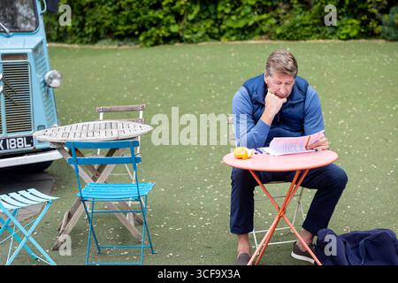 Londres, Royaume-Uni, 17 mai 2025, homme lisant des documents à la table de café en plein air avec orange et camionnette vintage en arrière-plan Banque D'Images