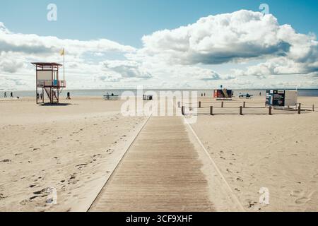 Large plage de sable avec une passerelle en bois menant au rivage. Il y a des postes de sauveteurs et des gens marchant le long de la plage Banque D'Images