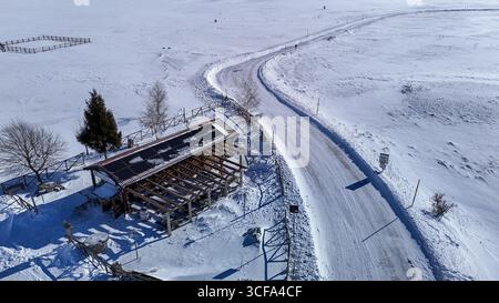 Paysage hivernal présentant une structure rustique à côté d'une route sinueuse dans un cadre rural enneigé pendant la lumière du jour Banque D'Images