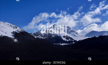 Les majestueuses montagnes enneigées se prélassent dans le ciel ensoleillé tandis que les nuages dansent gracieusement dans le bleu vif Banque D'Images