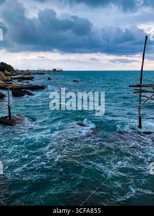Jetée de pêche trabocco en bois s'étendant au-dessus des eaux turquoises de l'Adriatique, ciel nuageux suspendu au-dessus de la côte rocheuse des Abruzzes près de Rocca San Giovanni Banque D'Images