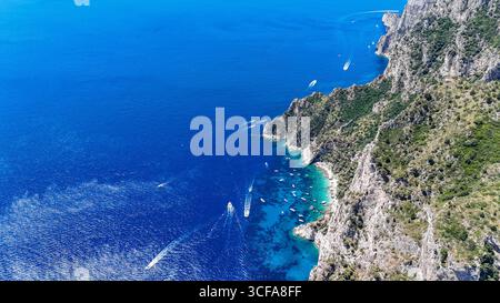 Les eaux d'Azur embrassent des falaises accidentées tandis que les bateaux dérivent près des rives tranquilles d'un paradis méditerranéen à midi Banque D'Images
