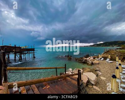 Passerelle en bois altérée passant près de la plate-forme de pêche de trabocco, nuages de tempête spectaculaires qui planent sur la côte adriatique dans les Abruzzes, en Italie Banque D'Images
