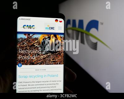 Dans cette illustration de photo, une personne tient un téléphone portable avec la page Web de la société américaine commercial Metals Company (CMC) sur l'écran devant le logo. Banque D'Images