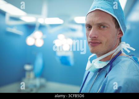 Chirurgien masculin debout sous les lumières chirurgicales dans OU portant le capuchon du masque de stéthoscope de gommage, espace de copie Banque D'Images