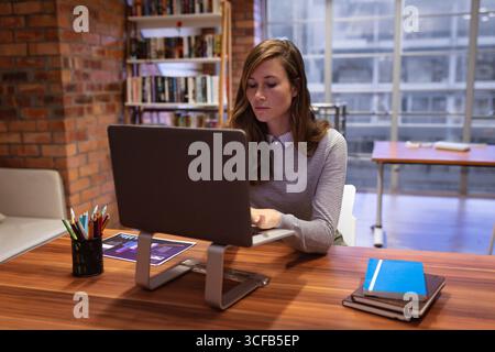 Ordinateur de bureau assis sur un bureau en bois avec un graphique imprimé à crayon et des cahiers près de la fenêtre Banque D'Images
