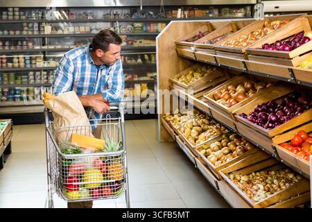 Homme adulte à mi-hauteur appuyé sur le chariot avec les bacs de fruits et légumes à l'ananas dans l'allée du supermarché, espace de copie Banque D'Images