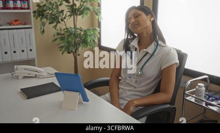 Femme se reposant en clinique avec stéthoscope autour du cou, tablette sur le bureau et dossiers en arrière-plan, illustrant la relaxation pendant le travail dans un se de soins de santé Banque D'Images