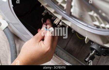 La main du maître retire les puces électriques pour retirer l'élément chauffant de la machine à laver et le capteur de chauffage. Réparation du lavage mac Banque D'Images