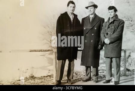 Vieille photo de groupe en noir et blanc de trois hommes debout sur la rive d'un bayou par une froide journée d'hiver - Novi Sad, Voïvodine, Serbie, Yougoslavie, années 1960 Banque D'Images