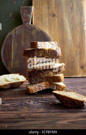 Nature morte rustique avec des tranches empilées de pain artisanal, des tomates cerises dans un bol en bois et des planches de cuisine de ferme. Concept de slow food confortable Banque D'Images