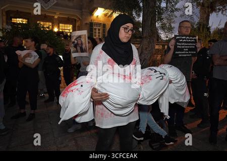 HAÏFA, ISRAËL - 21 AOÛT : les manifestants tiennent des colis enveloppés dans des enveloppes, symbolisant les corps d'enfants palestiniens tandis que d'autres manifestants arabes israéliens et militants pour la paix tiennent des pancartes condamnant la guerre, aux côtés de photos d'enfants palestiniens et de journalistes tués par l'armée israélienne à Gaza lors d'une manifestation contre la guerre israélienne dans la bande de Gaza le 21 août 2025 à Haïfa, Israël. Banque D'Images
