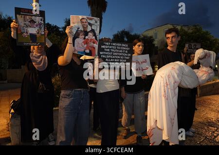 HAÏFA, ISRAËL - 21 AOÛT : les manifestants tiennent des colis enveloppés dans des enveloppes, symbolisant les corps d'enfants palestiniens tandis que d'autres manifestants arabes israéliens et militants pour la paix tiennent des pancartes condamnant la guerre, aux côtés de photos d'enfants palestiniens et de journalistes tués par l'armée israélienne à Gaza lors d'une manifestation contre la guerre israélienne dans la bande de Gaza le 21 août 2025 à Haïfa, Israël. Banque D'Images