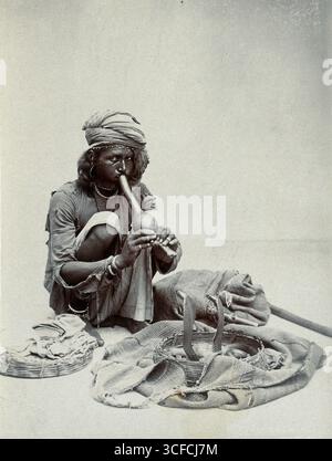 Un charmeur de serpent indien accroupissant en jouant sa pipe, avec deux cobras dans un panier devant lui, dans un studio, c1900. Banque D'Images