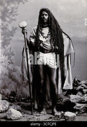 Un Indien aux cheveux longs, portant un bâton, dans un studio, 1900. Banque D'Images