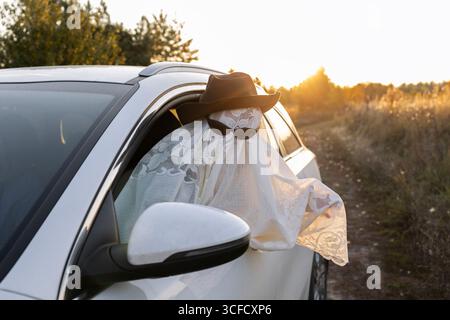 enfant dans une couverture blanche et des lunettes noires penché par une fenêtre de voiture contre un coucher de soleil orange. Trick or Treat. Concept d'Halloween. Créativi des enfants Banque D'Images