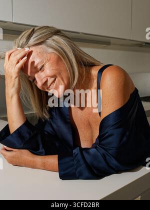 Femme souriante aux cheveux courts portant une robe sombre, appuyée sur un comptoir de cuisine. Italie Banque D'Images