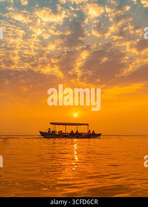 Touristes silhouettés dans un Longboat sur le fleuve Gange au lever du soleil à Varanasi, Inde, sous un ciel dramatique. Banque D'Images